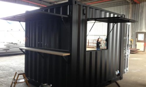 Black shipping container kiosk with two serving windows
