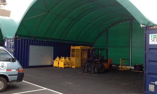 Shipping container shelter with roller door and forklift under canopy