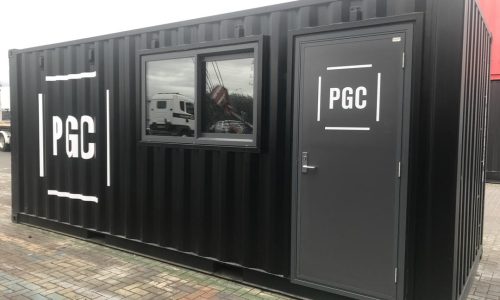 Black shipping container, modified with a window and door to be a site office. Branded with PGConstructors
