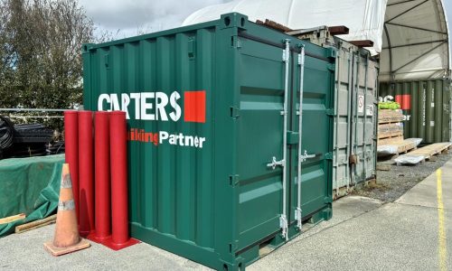 Small 8ft green shipping container branded with Carters, next to a container shelter